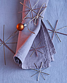 Weihnachtsdeko mit Stoffserviette, Silbersternen und kupferfarbener Christbaumkugel