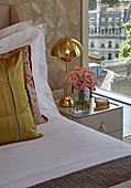 Goldene Nachttischleuchte und Strauß Rosen neben dem Bett