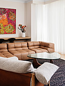 Leather sofa and coffee table with glass top in front of window with floor-length curtain