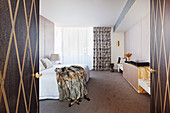 View through open double door to double bed with fur blanket in elegant bedroom
