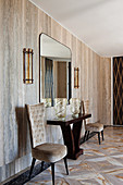 Console table with glass vases, chairs and wall mirror in elegant hallway with travertine wall covering