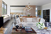 Coffee table made of ebony and brass, next to it a bouquet of flowers on a marble coffee table, in the background a bright sofa in an open living room