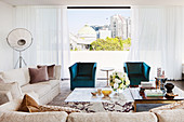 Marble coffee table next to ebony and brass coffee table, elegant sofa set and turquoise armchair in front of window in penthouse apartment