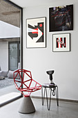 Red designer chair with cement pedestal and side table below modern artworks on wall