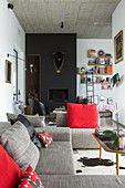 Grey sofa set with red scatter cushions in front of bull's head on black wall above fireplace
