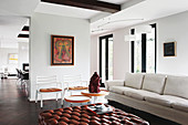 Pale sofa, sculpture on side table, chairs and leather ottoman in lounge area