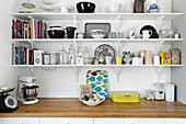 Crockery and kitchen utensils on three shelves above worksurface