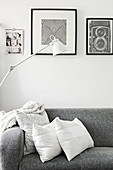 Cushions on grey sofa below black and white pictures and standard lamp
