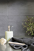 Soap dispenser, tea towel and washing-up brush in front of grey wall tiles