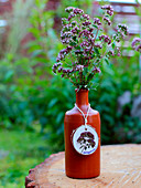 Flowering oregano in clay bottle with tag made from wooden disc