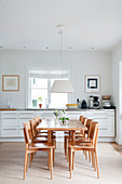 Stühle und Esstisch aus hellem Holz vor weißer Küchenzeile