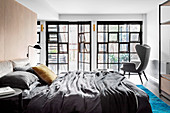 Doppelbett und Ohrensessel im Schlafzimmer mit Industriefenster und Terrassentür