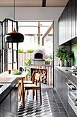 Black kitchenette, kitchen island and dining area, in the background pizza oven on the terrace