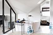 Free-standing bathtub in ensuite attic bathroom with glass wall