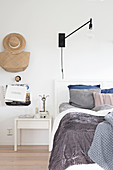 Grey bed linen and wall-mounted lamp in white bedroom