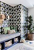 Sitzbank mit Polsterauflage und Kissen, Garderobenleiste mit Hüten und Zimmerpflanze vor tapezierter Wand