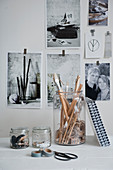 Office utensils in glass jars in front of black and white photos on wall