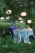 Set table and chair with matching covers below illuminated lanterns in garden