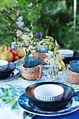 Table set in shades of blue with glasses in raffia holders in garden