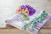 Primulas and roses in glass of water on cloth with pompom trim