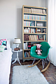 Green designer rocking chair in front of bookcase in bedroom