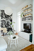 Round white side table on pale rug, TV cabinet, wall-mounted shelves and two chairs against large poster in living room