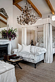 Four-poster bed and pale grey couch in elegant, classic bedroom