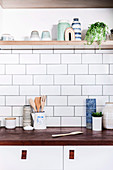 Kitchen utensils on wooden worktop, white wall tiles and shelf above