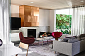 Loungebereich mit Designer-Sitzmöbeln und Kamin, darüber Kupferplatte
