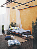Loungers with mattresses and cushions on terrace next to yellow exterior wall