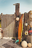 Surfboard leaning against fence next to outdoor shower and buoys