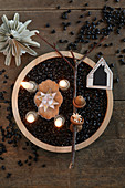 Advent arrangement of four lit candles amongst black beans in wooden dish