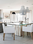 White upholstered chairs around modern glass and wood dining table
