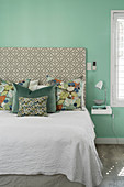 Scatter cushions with various patterns on bed against mint-green wall