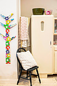 Stilisierter Baum aus Sperrholz mit bunter Folie beklebt an Wand, Stuhl mit Kissen und cremefarbener Küchenschrank