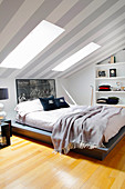 Doppelbett im Dachzimmer, grau-weiß gestreifte Tapete an der Decke