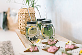 Triangular open faced sandwiches and flavoured water in mason jars with handles on buffet