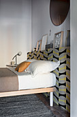 Bed against protruding wall section covered in patterned wallpaper