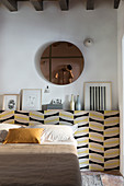 Round mirror above protruding wall section used as bed headboard
