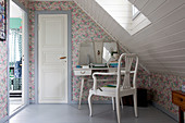 Typewriter on vintage desk and chair in attic room with floral wallpaper