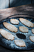 Leaf-shaped biscuits dusted with icing sugar on tray