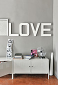 Lettering spelling 'LOVE' on grey wall above white metal sideboard