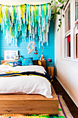 Doppelbett mit Holzgestell vor blauer Wand, darüber bunte Wimpelkette