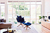 Designer armchair with footstool in front of glass front in bright living room