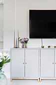 Candles on pale grey base units below TV mounted on wall
