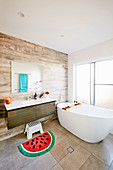 Freestanding bathtub in front of sliding glass door, vanity and bath mat with melon motif in the bathroom