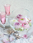 Hochzeitsdekoration: Glasschale mit Blüten, Sektgläser und Besteck auf einem Tisch