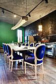 Antique chairs with velvet upholstery around long dining table in front of kitchen counter in renovated loft apartment