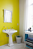 Pedestal sink and mirror on yellow wall in bathroom