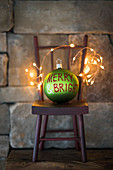 Green Christmas bauble and fairy lights on miniature chair